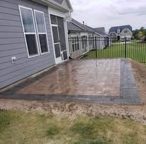 Gray house with a paved patio. Grass and a fence are also visible.