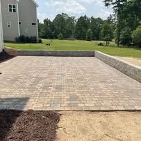 Brick patio with retaining wall, surrounded by green grass and a house.
