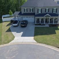 A large, two-story house with a driveway and parked vehicles, surrounded by green grass and trees.