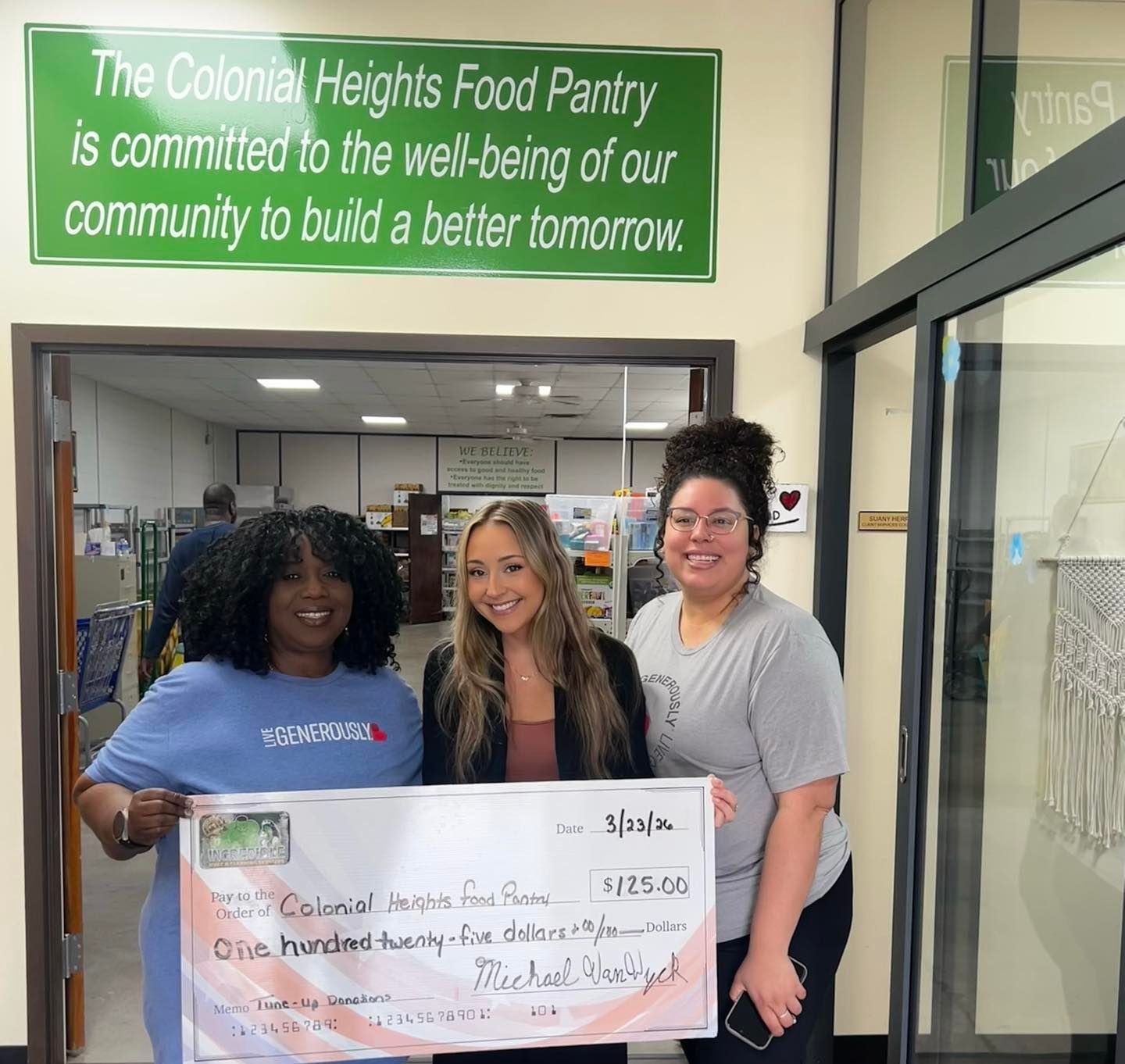Man and young woman holding a large check, smiling in front of painted fruit on a wall.