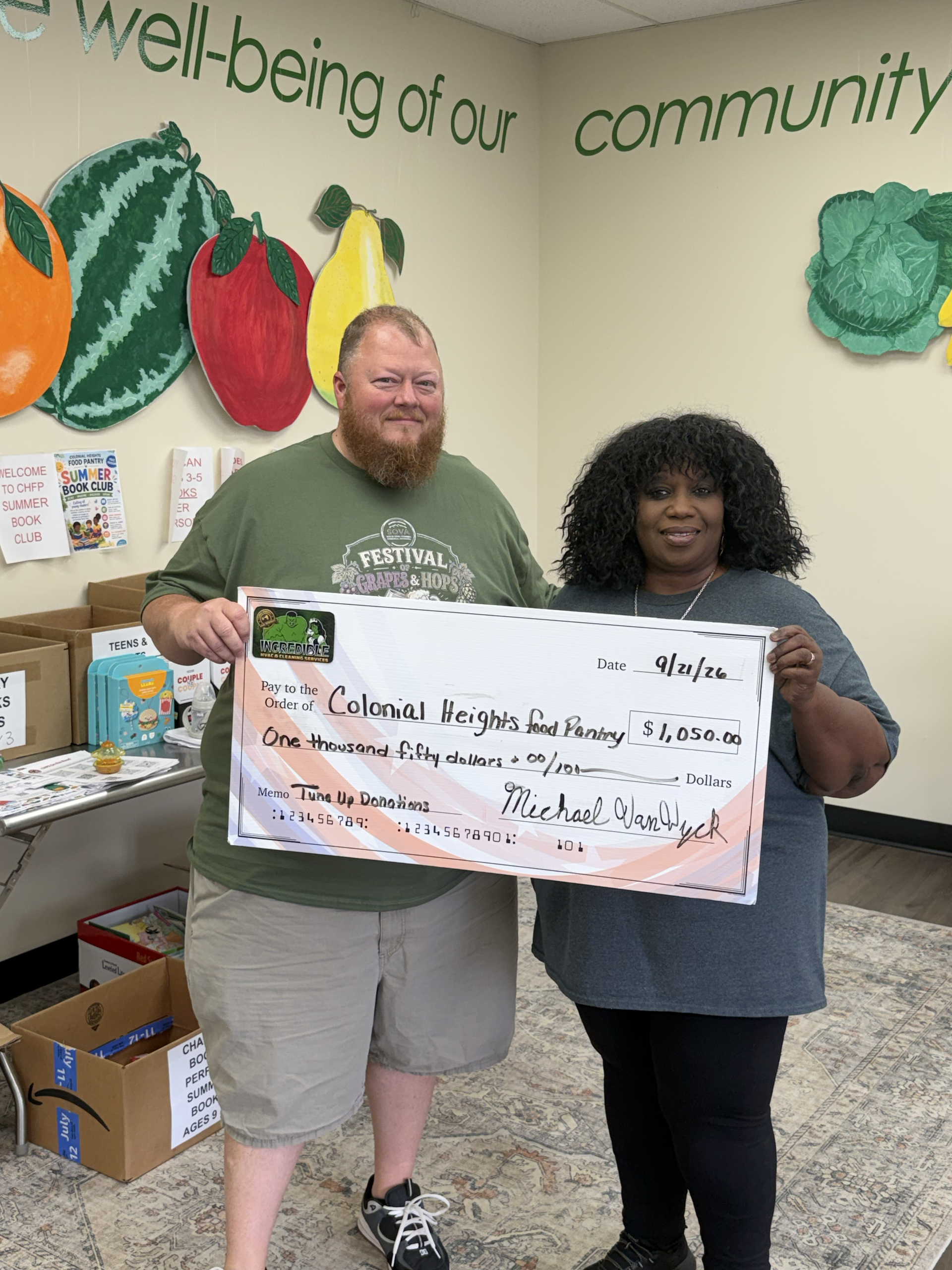 Two people hold a large ceremonial check in a community center with produce murals in the background.