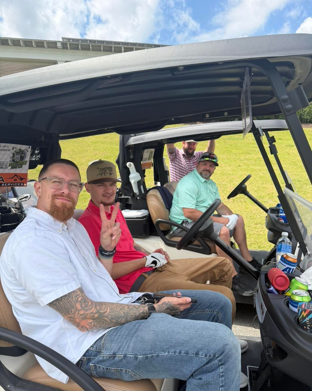 Four people sitting in a golf cart, smiling and waving outdoors on a sunny day.