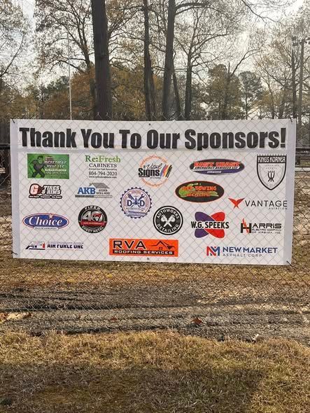 A white sponsorship banner attached to a chain-link fence, listing various business logos under the title 