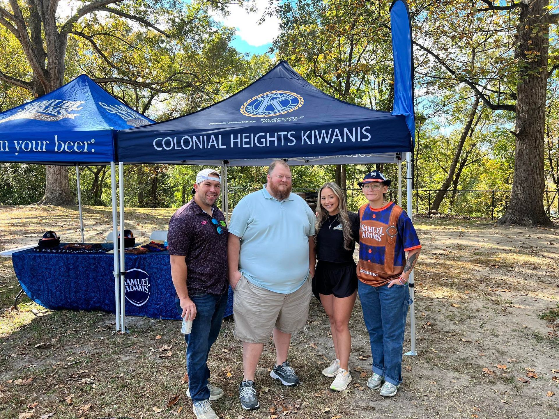 Four people pose in front of a Colonial Heights Kiwanis tent at an outdoor event.