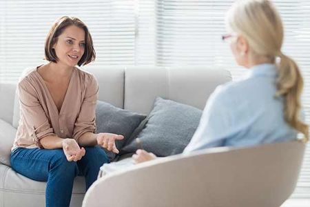 A woman is sitting on a couch talking to a therapist.