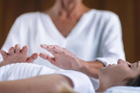 A woman is laying on a bed getting a healing session.