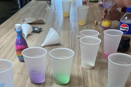 A person is pouring liquid into plastic cups on a table.