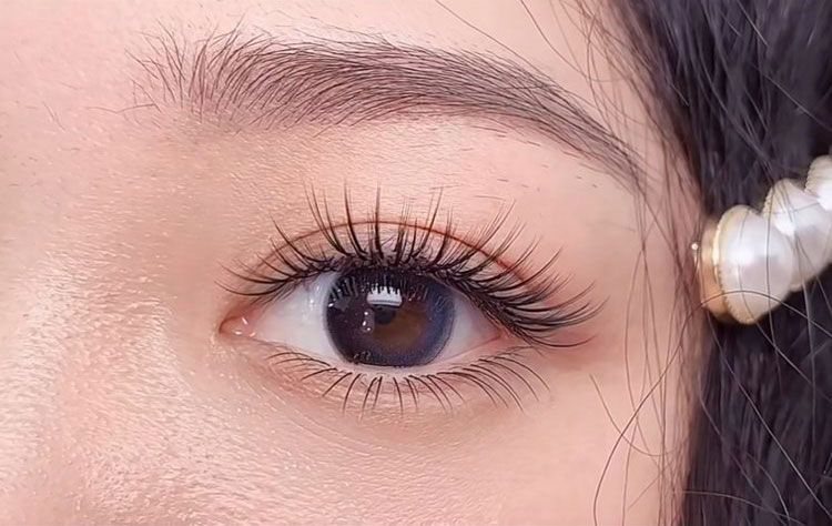 A close up of a woman 's eye with long eyelashes and a pearl necklace.