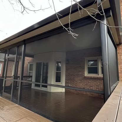 a screened in porch with a brick house in the background