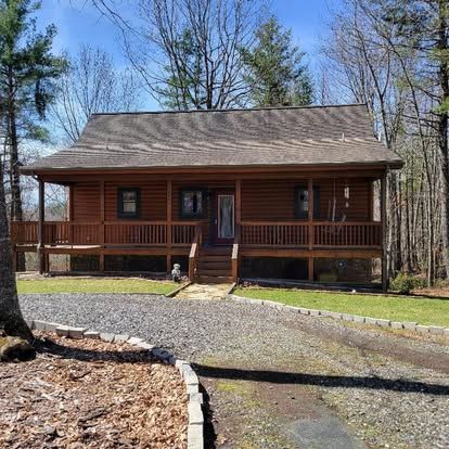 a log cabin with a large porch in the middle of the woods