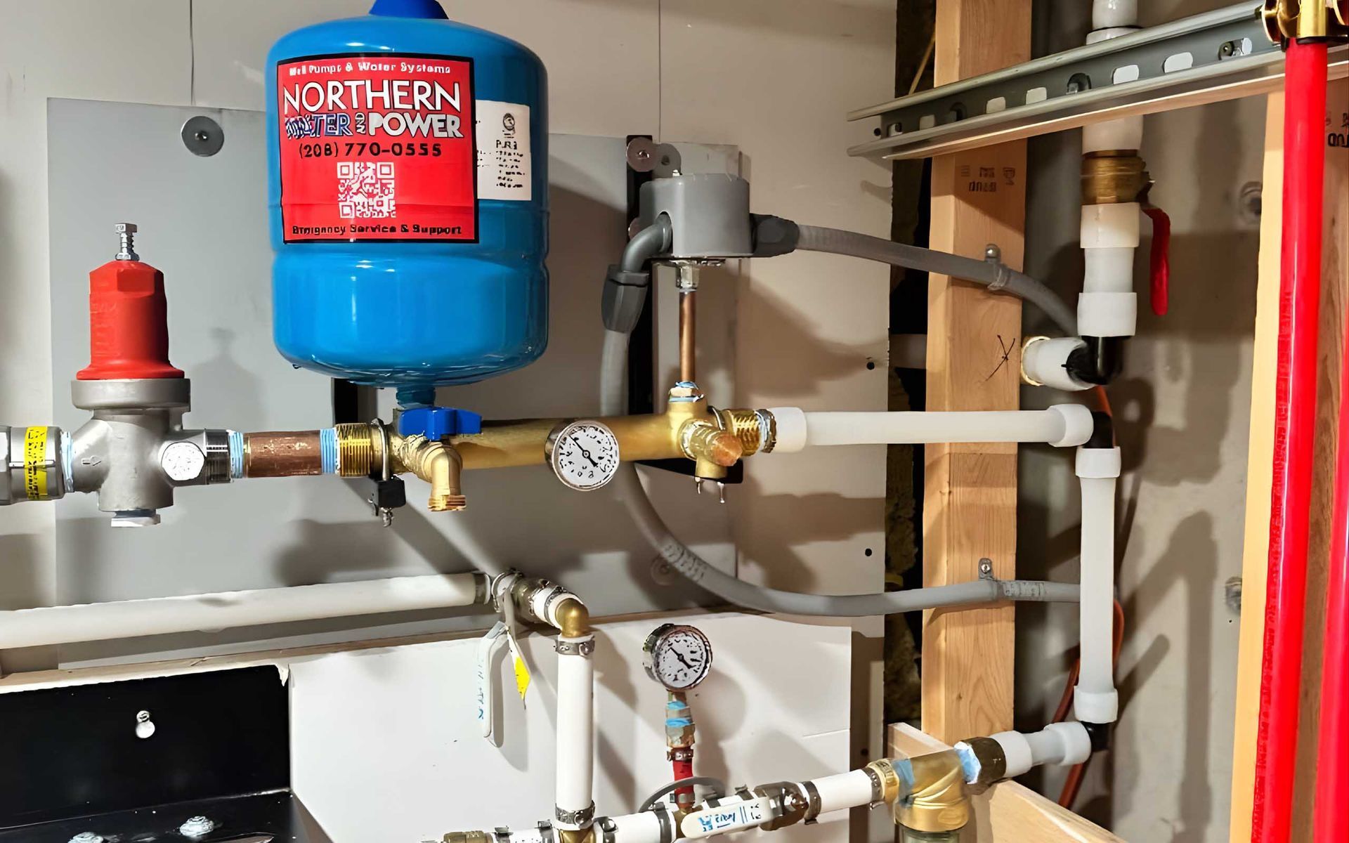 Blue expansion tank, brass valves, gauges, and white pipes against a wall.