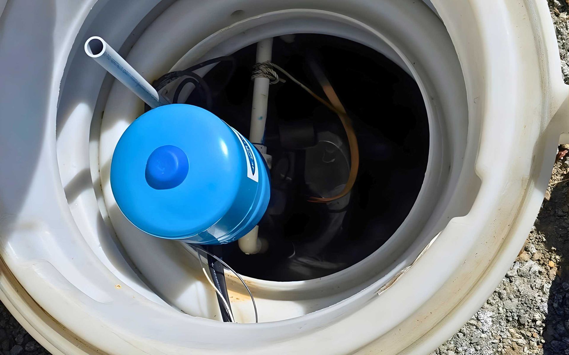 Overhead view inside a white tank, showing a blue pump and various pipes.
