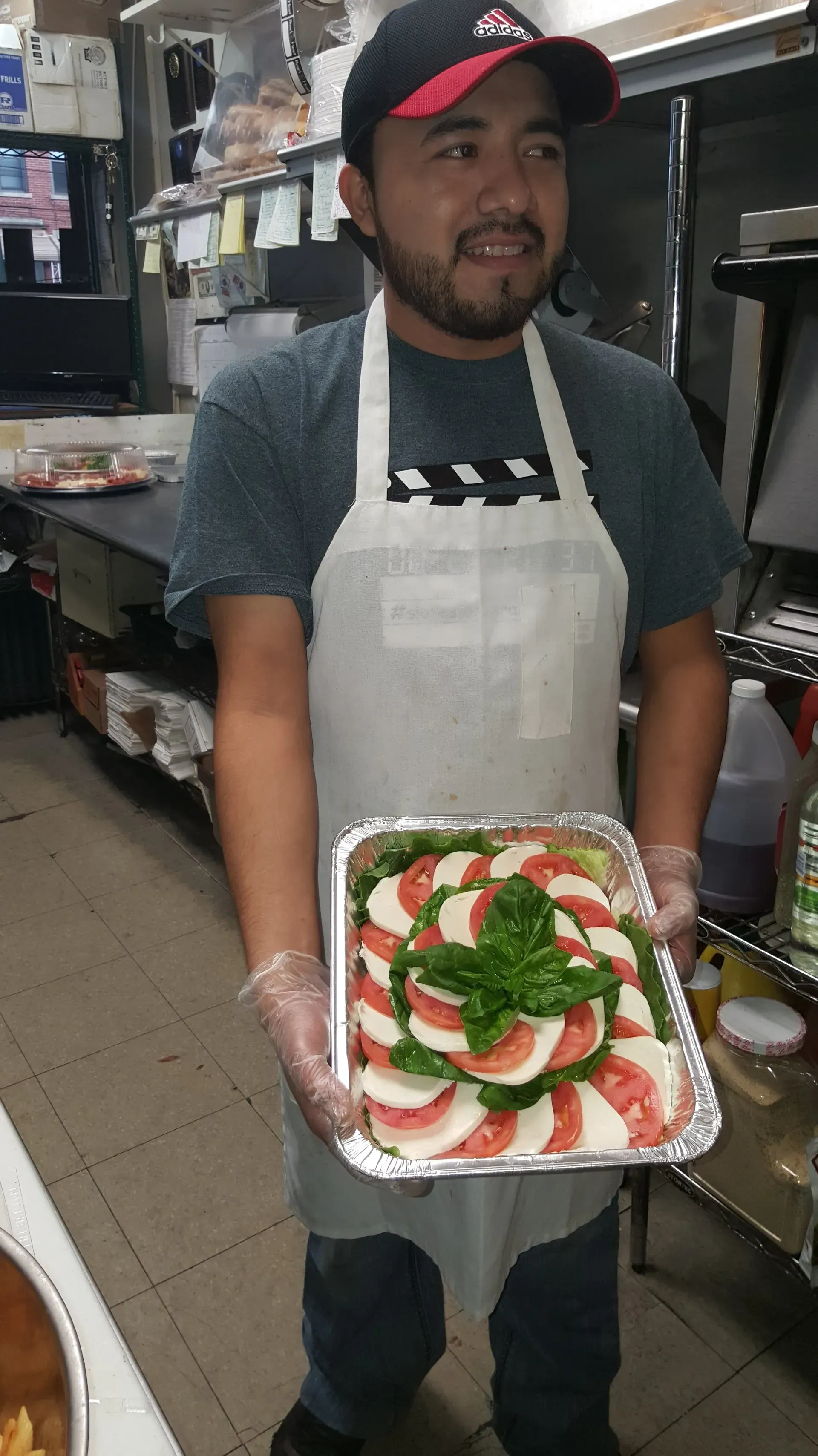 A man in an apron is holding a tray of food in a kitchen.