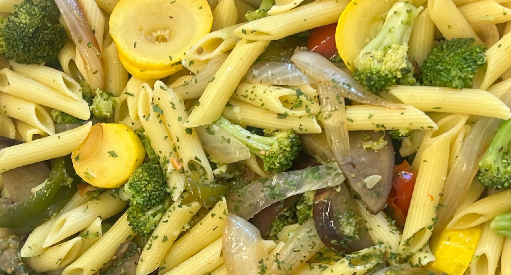 A close up of a pasta salad with broccoli, squash, tomatoes and onions.