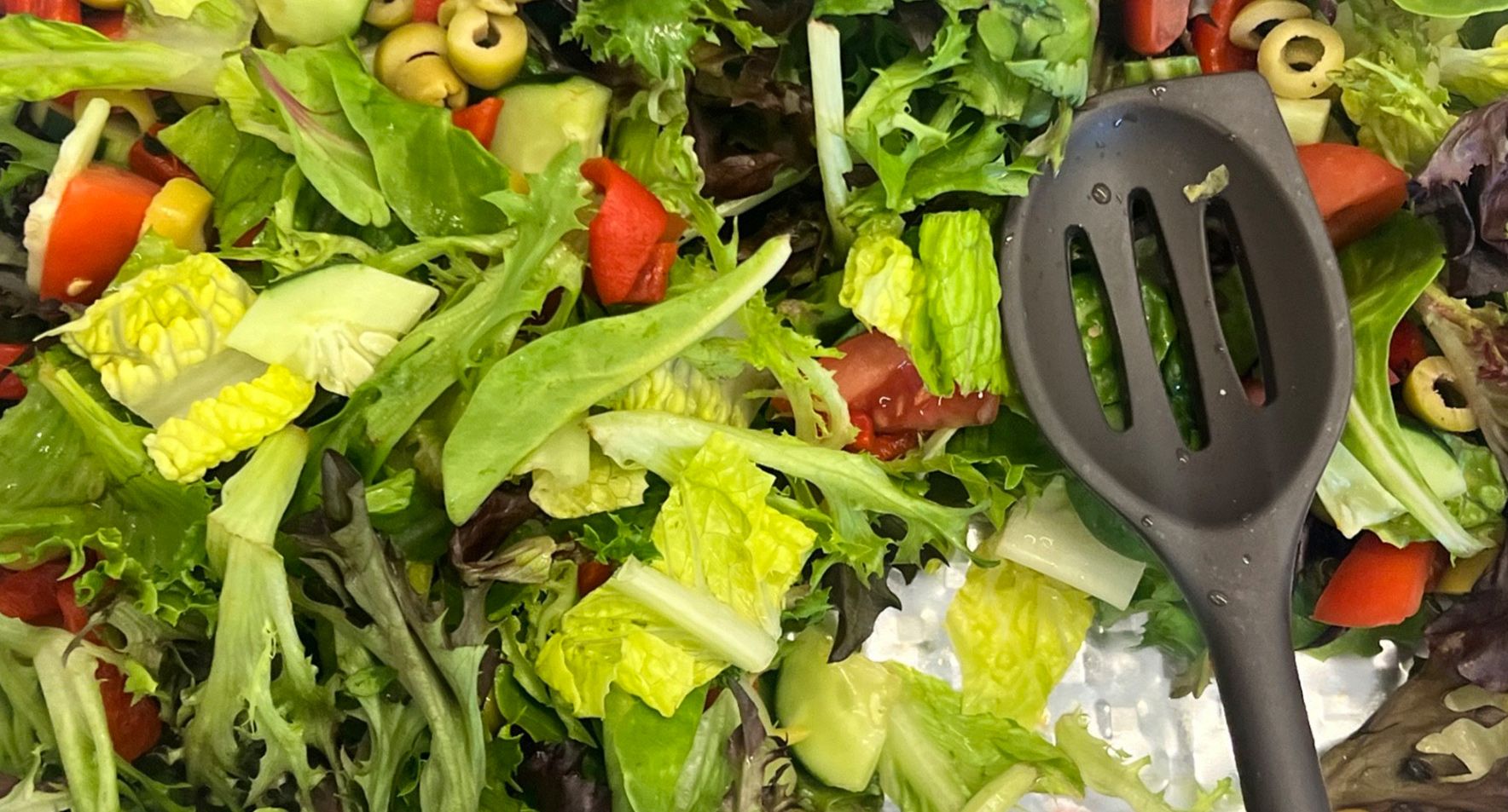 A close up of a salad with a spatula in it.