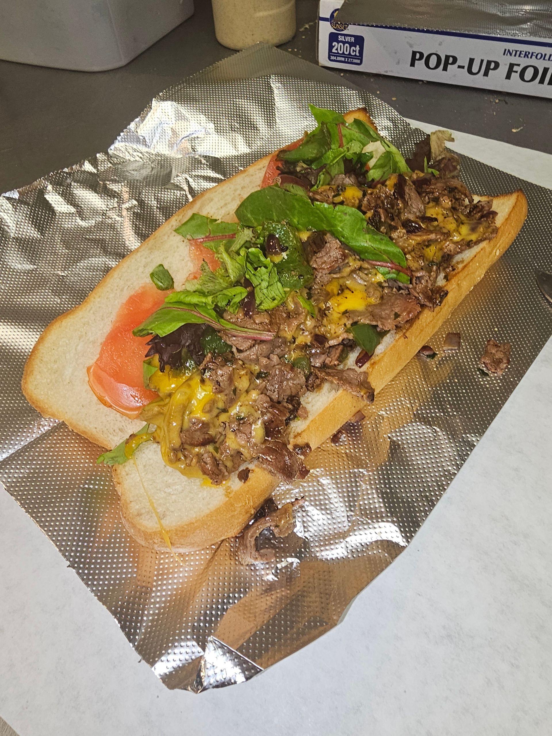 A steak sandwich is wrapped in tin foil on a table.