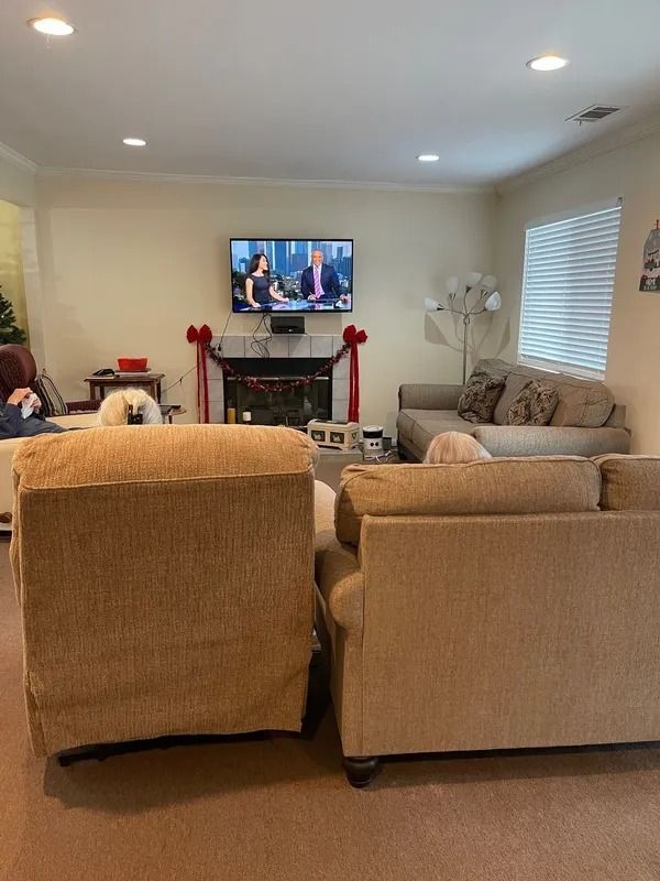 A living room with tan couches facing a TV above a fireplace decorated for the holidays.