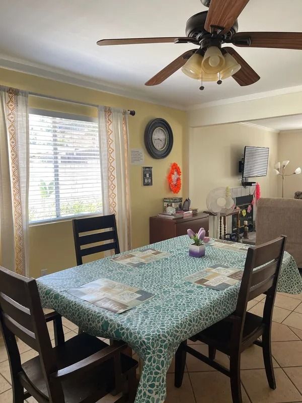 A dining room with a table set for four, next to a window with blinds. A ceiling fan hangs overhead.