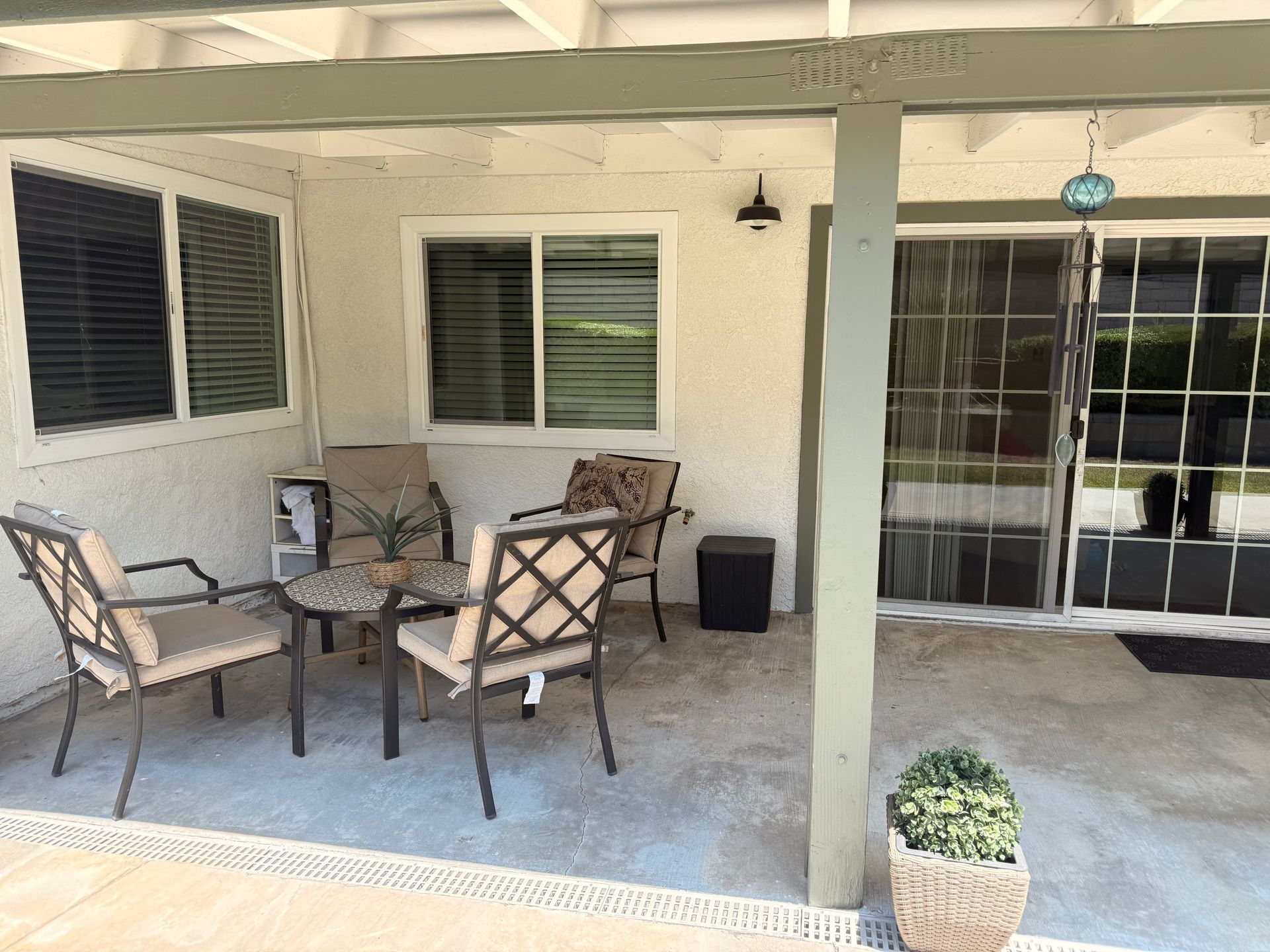 A covered patio with a seating area.  There are four chairs, a small table, and a potted plant.