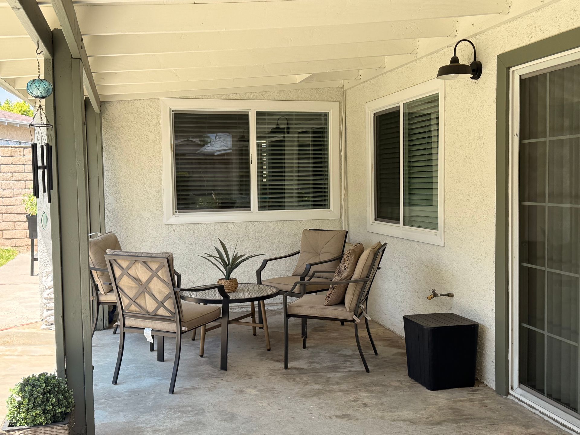 A patio with a small table, chairs, and a subwoofer. The space has a white ceiling, stucco walls, and a sliding glass door.