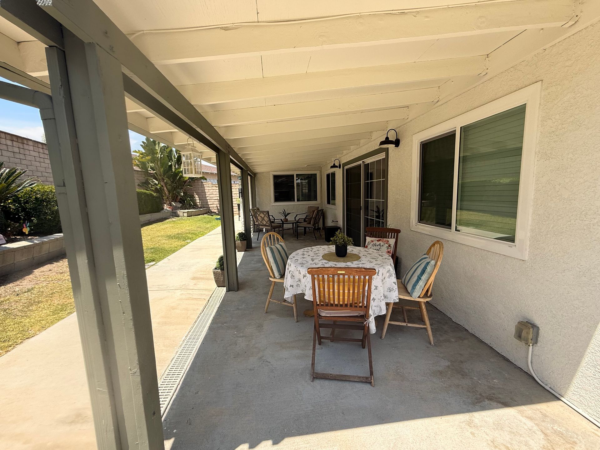 Covered patio with a dining table and chairs, next to a house with windows and a sliding door.
