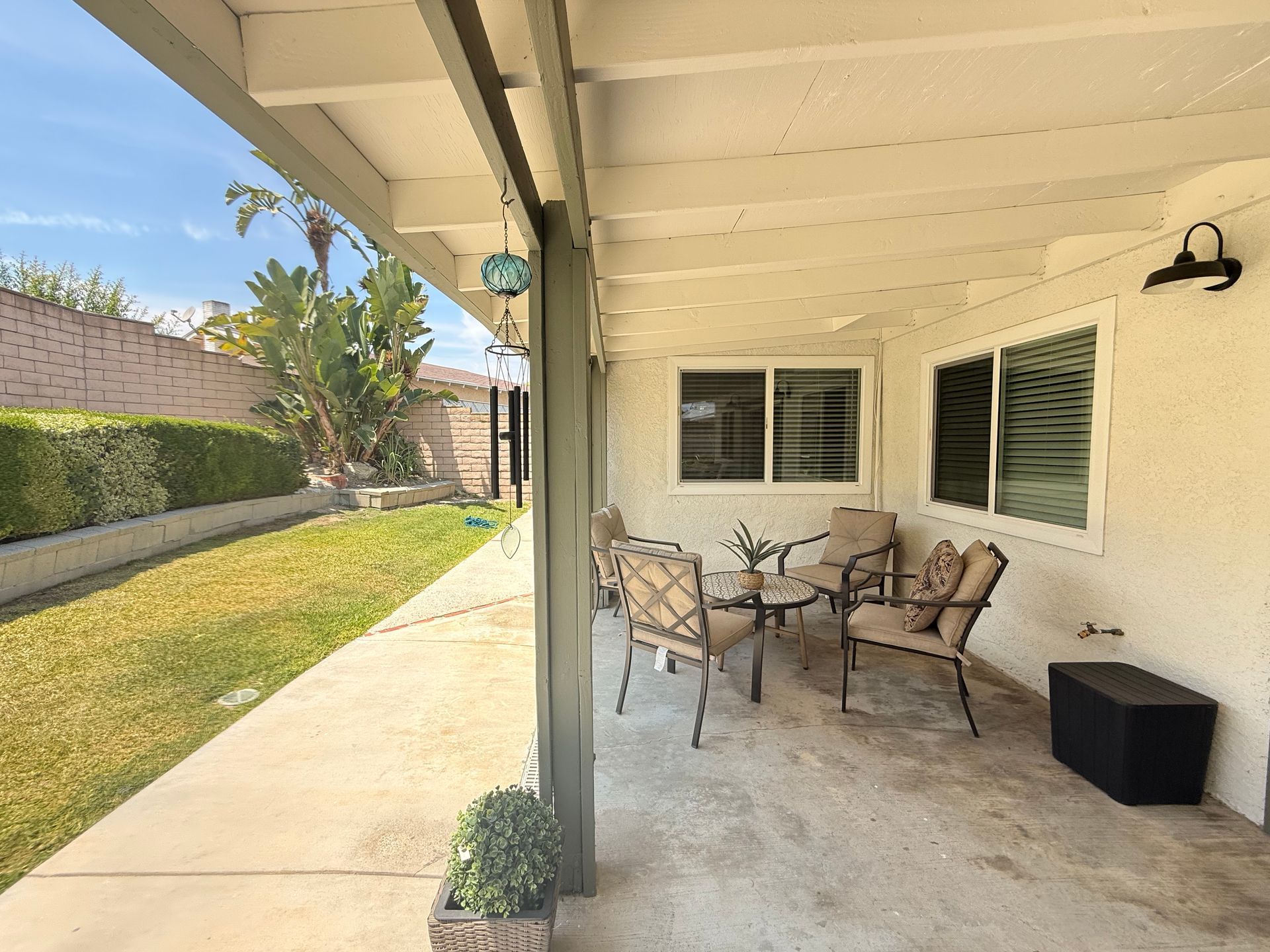 Covered patio with seating area overlooking a grassy backyard. Beige walls and ceiling with dark metal light fixtures.