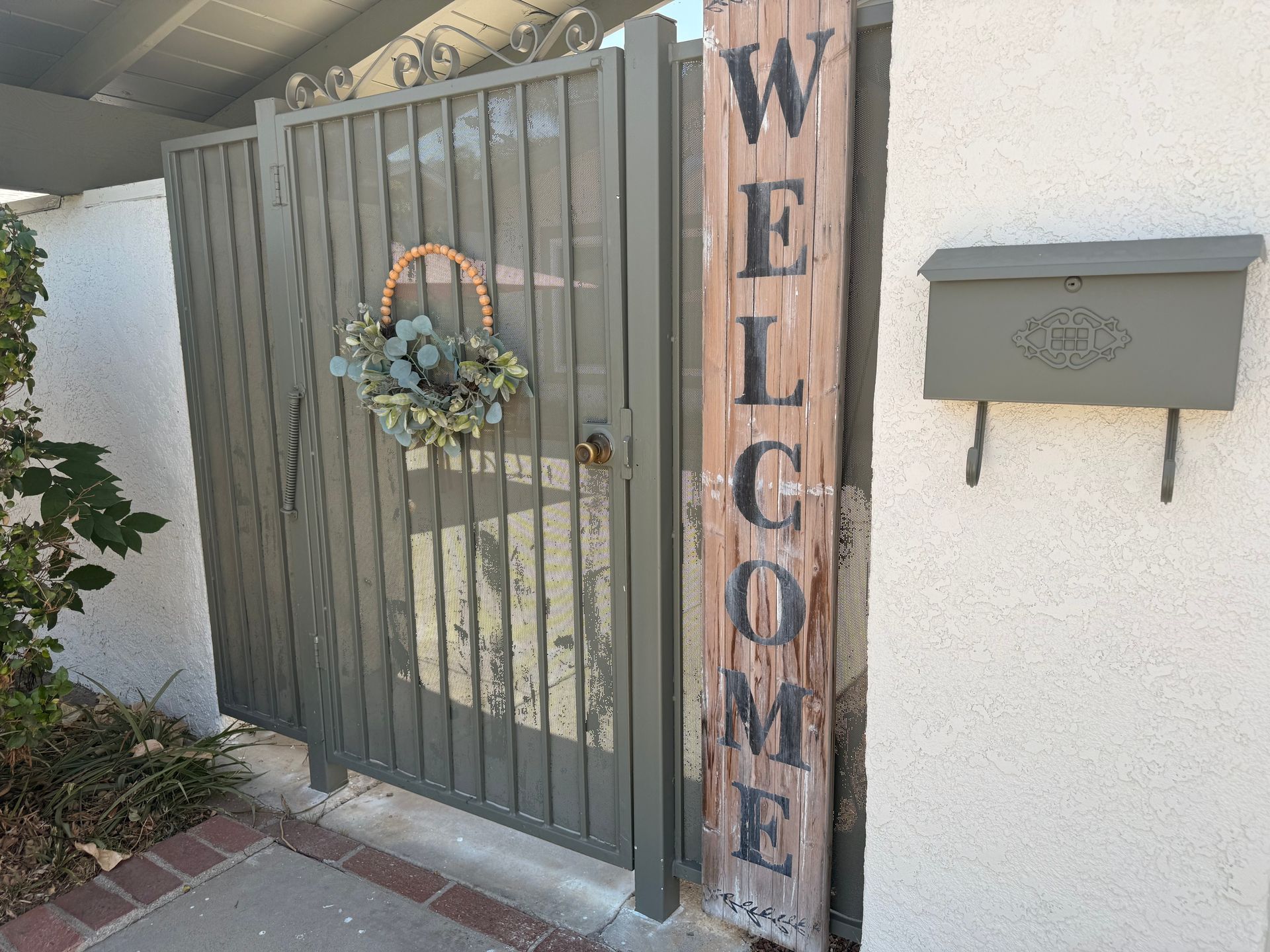 A weathered, green metal gate with a eucalyptus wreath, a 