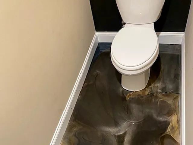 Small bathroom with a white toilet and a dark, water-damaged floor.