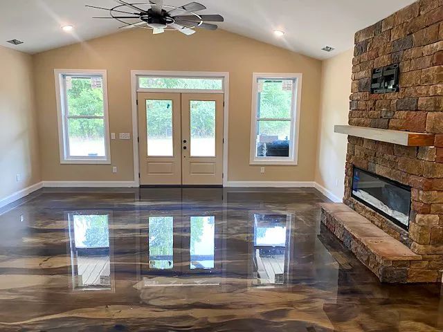 Empty living room with polished dark floor, beige walls, French doors, and a stone fireplace.