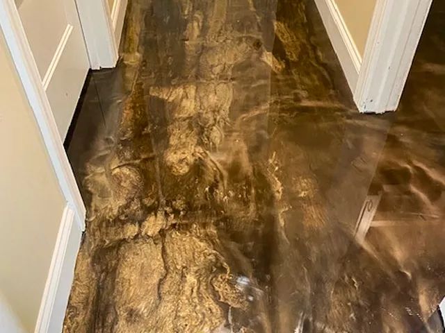 Water-damaged hallway floor with dark brown stains and peeling finish near white doorways