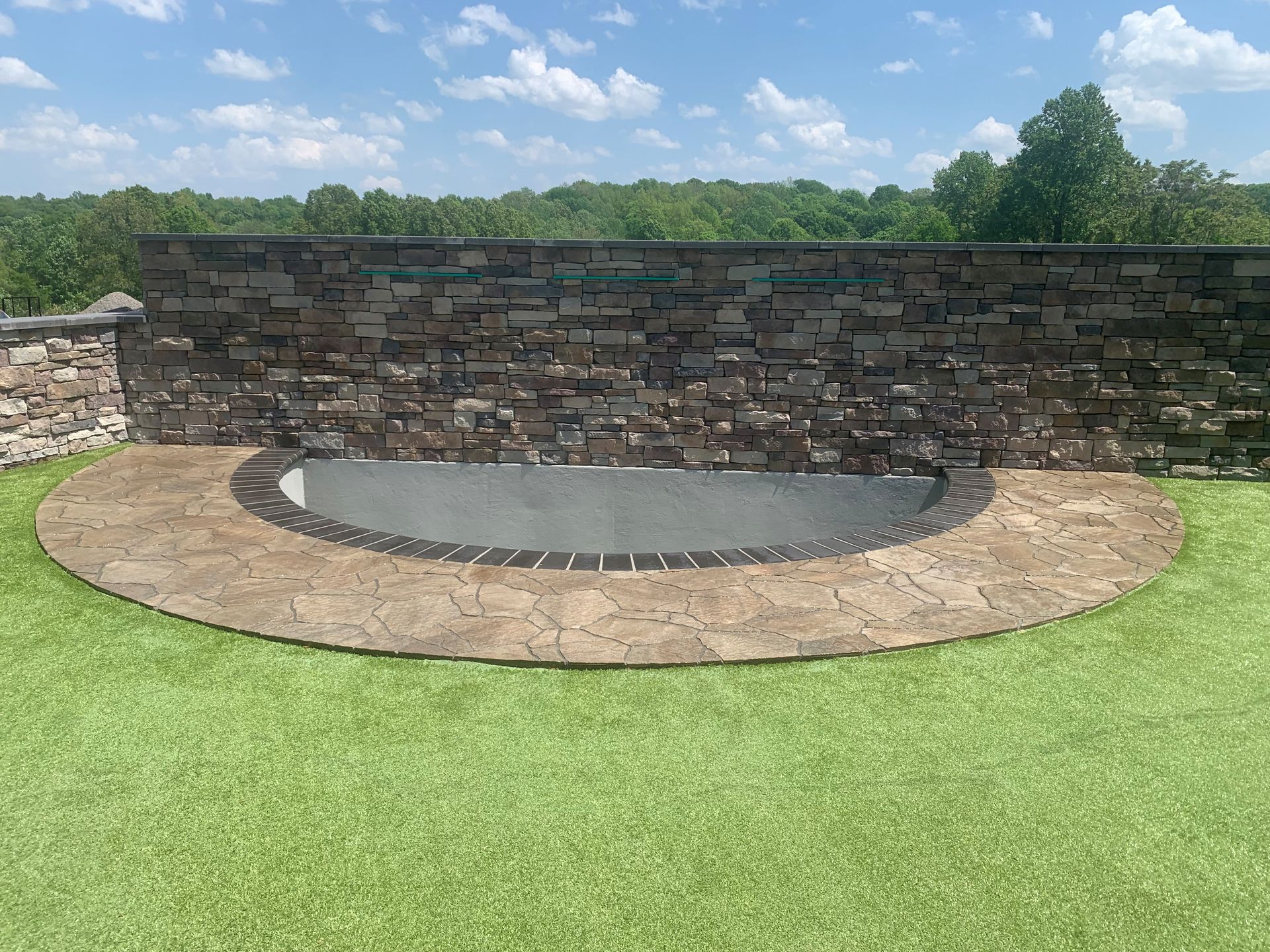 Stone fire pit with curved retaining wall in a grassy yard under a blue sky