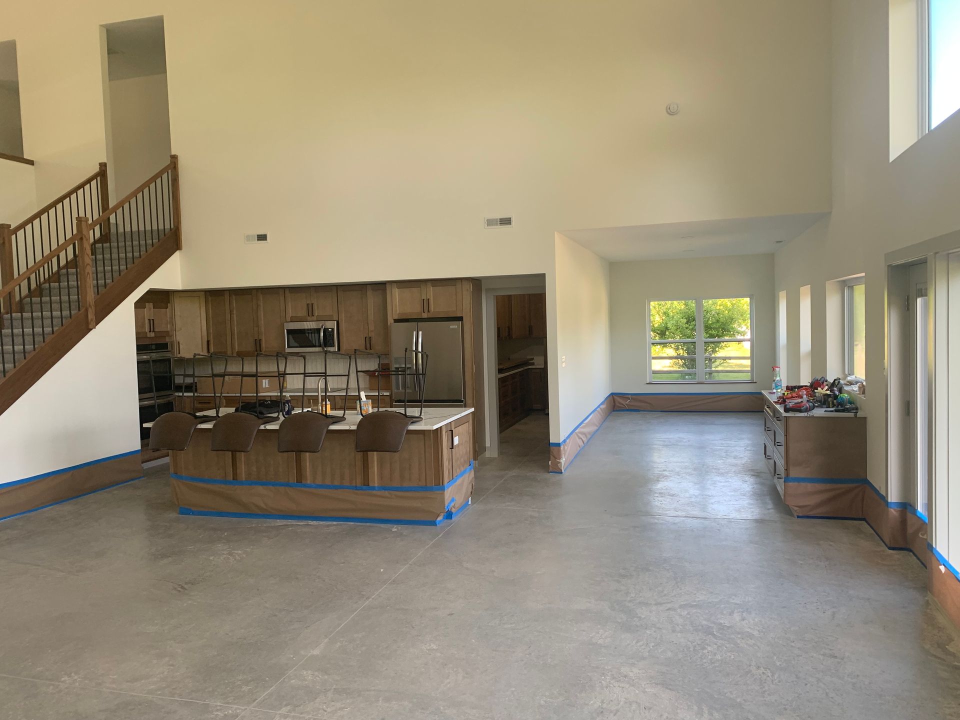 Large open room with a raised kitchen island, wooden cabinets, staircase, and windows along the right wall.