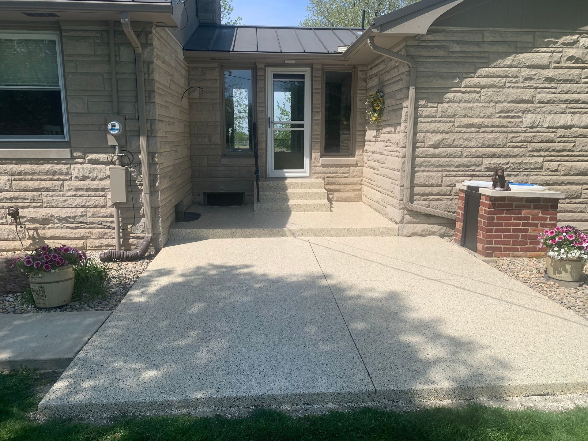 Front entrance of a stone house with concrete walkway, steps, and a glass door.