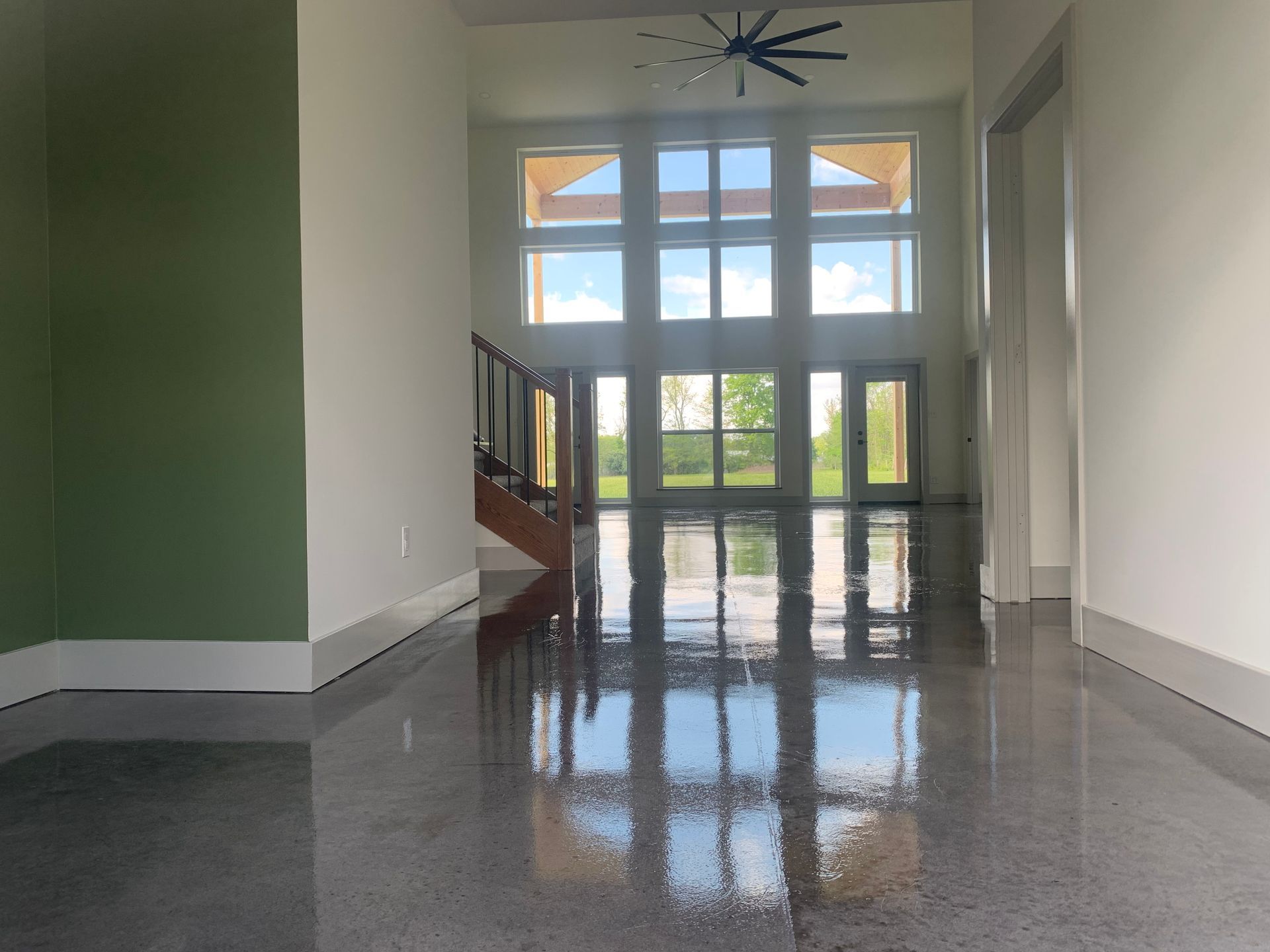 Empty modern hallway with glossy gray floor, white walls, green accent wall, and large glass doors at the end