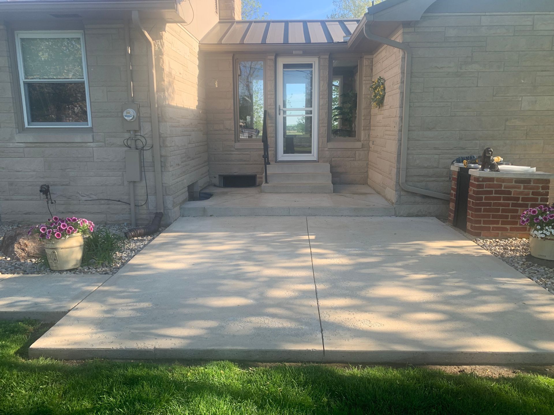 Stone house front entrance with a concrete walkway, potted flowers, and a small brick planter.