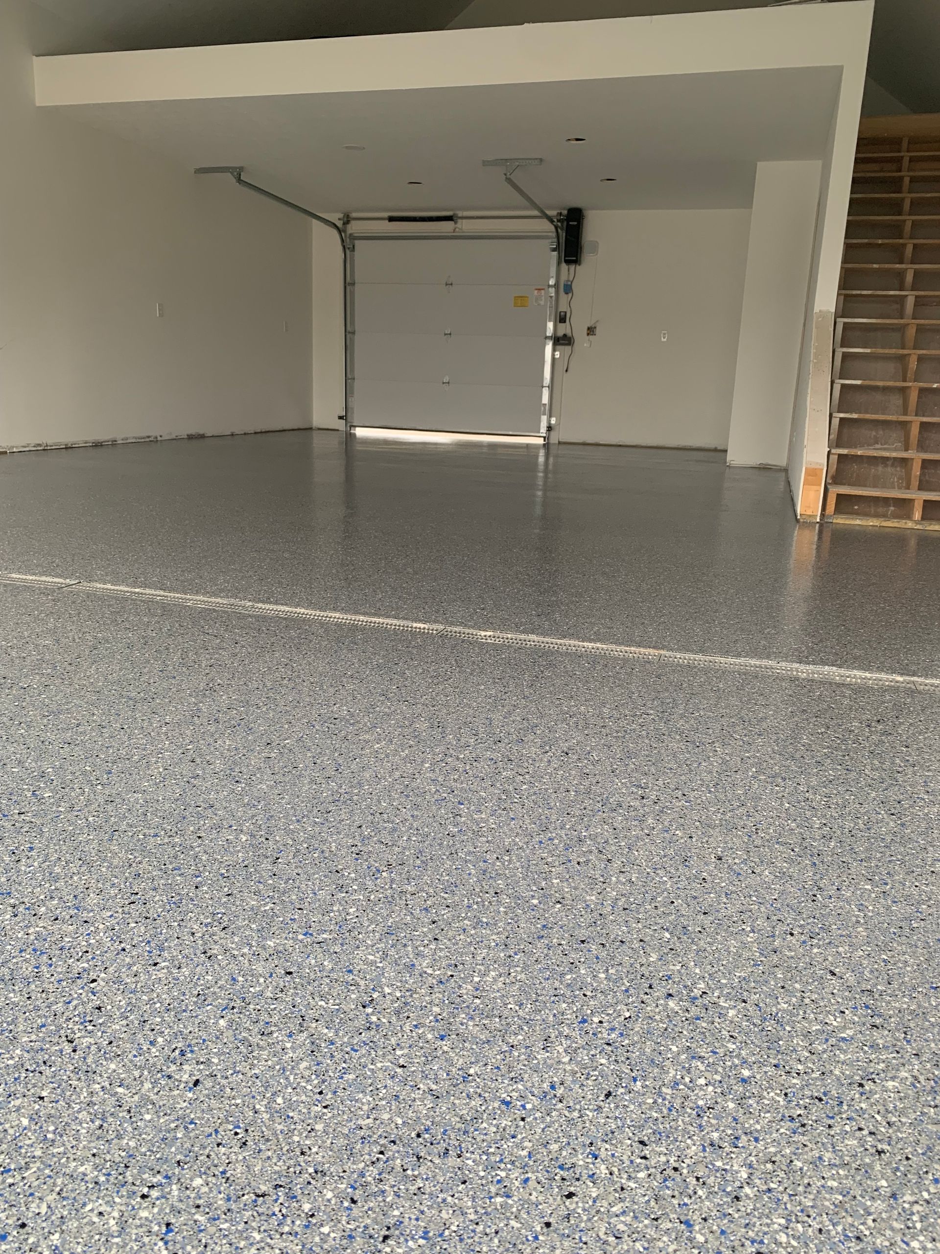 Empty garage interior with speckled gray epoxy floor and a closed white garage door.