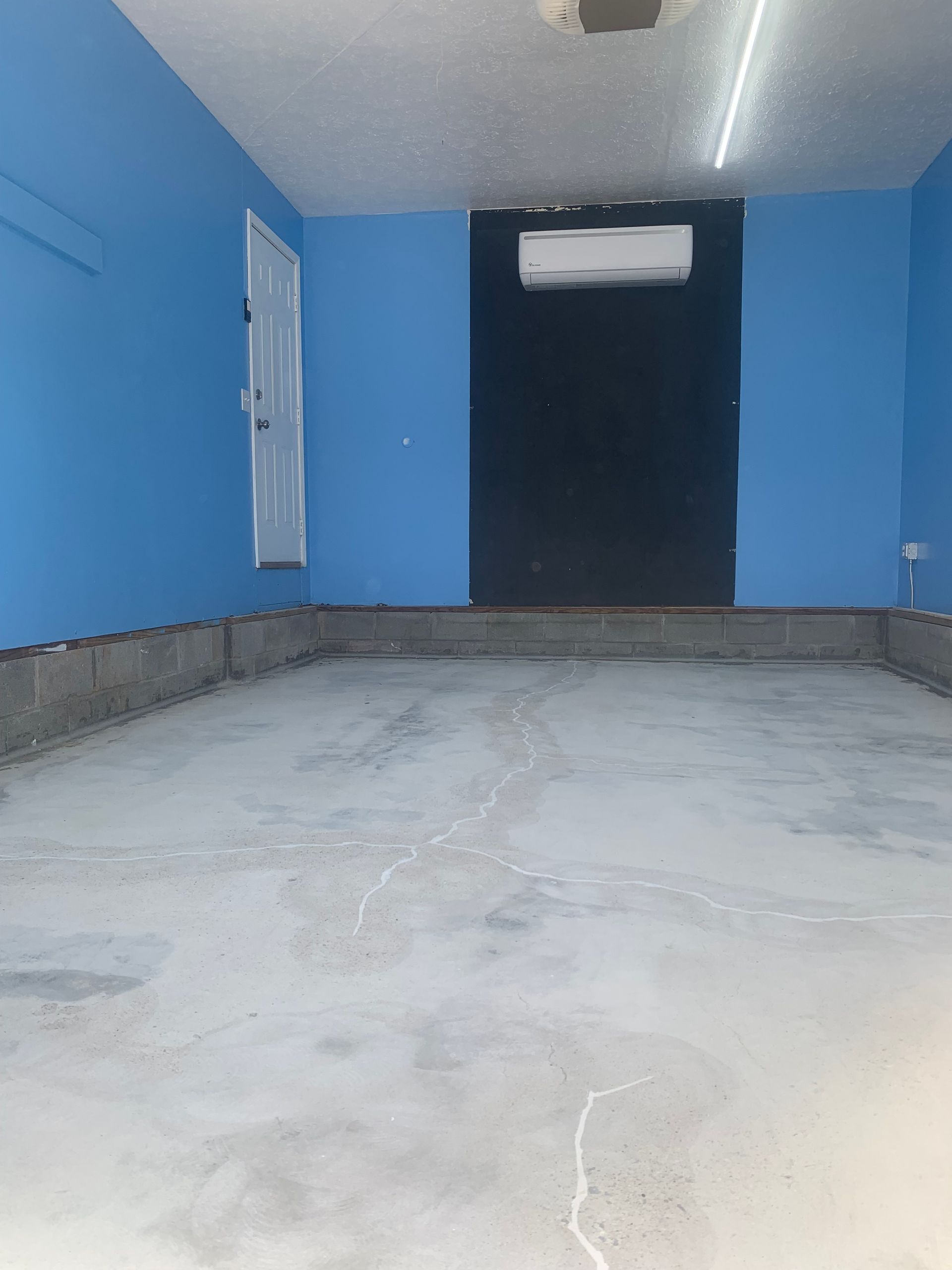 Empty blue room with a concrete floor, dark doorway, and wall-mounted air conditioner