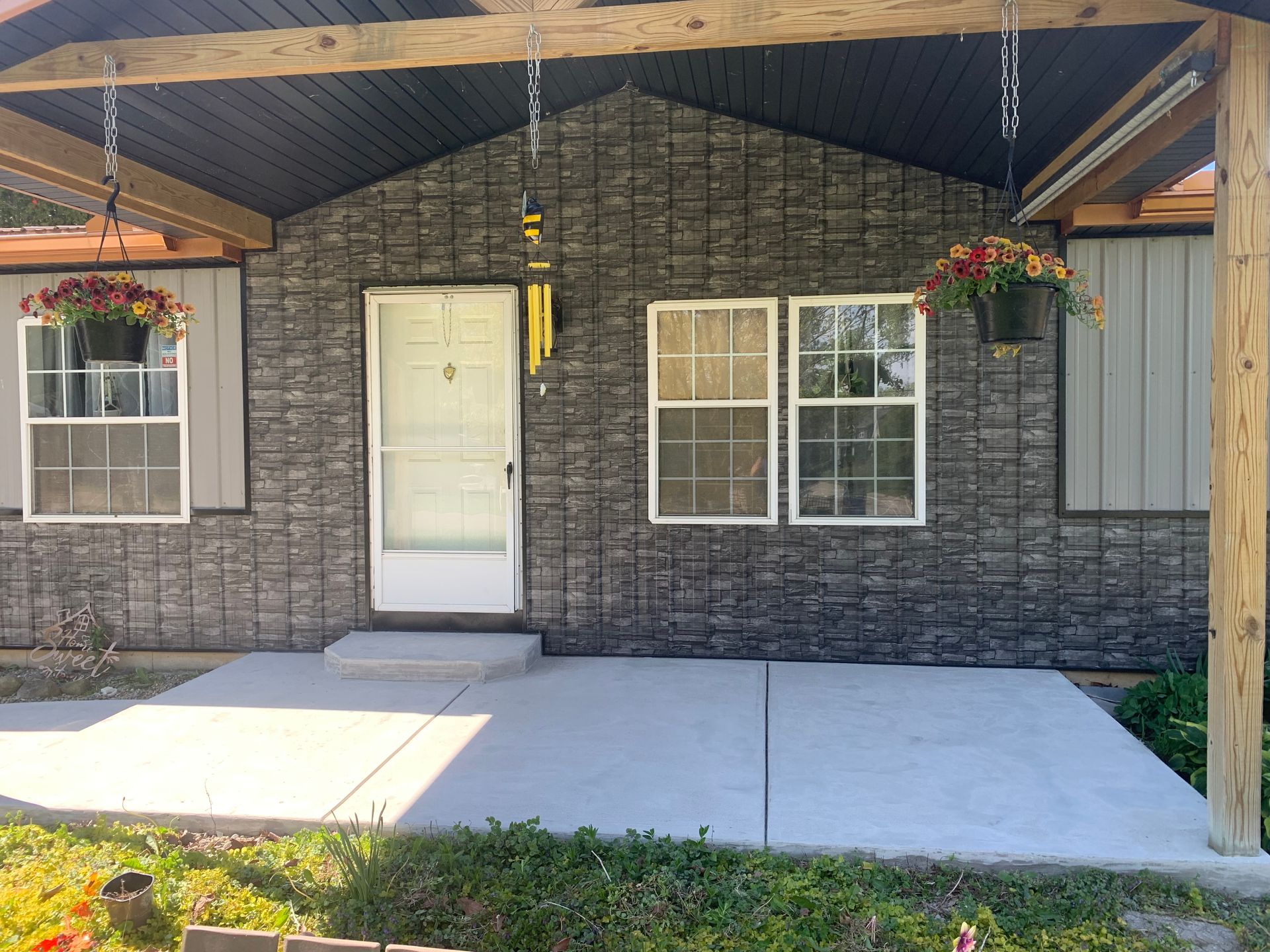 Front porch with gray brick facade, white door and windows, concrete walkway, and hanging flower baskets