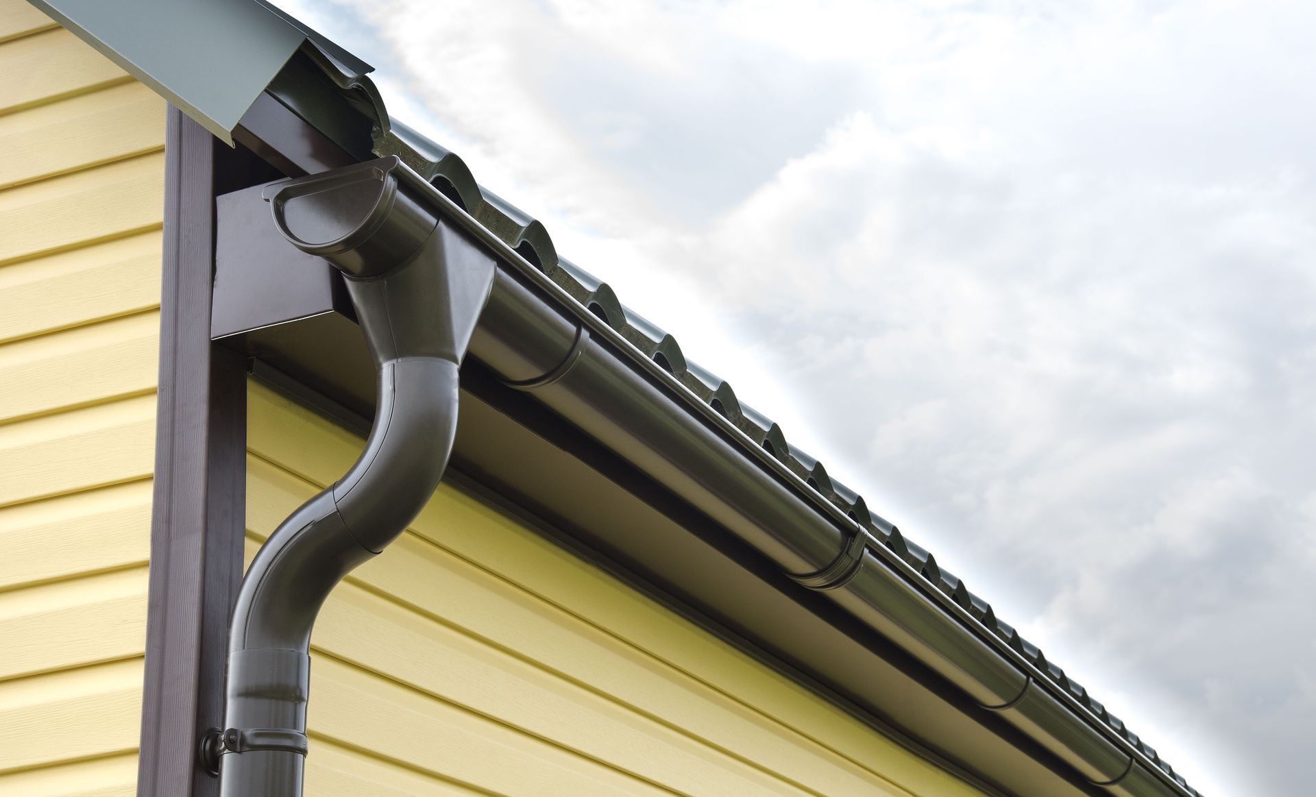 Brown gutters on a yellow house with a gray sky background.