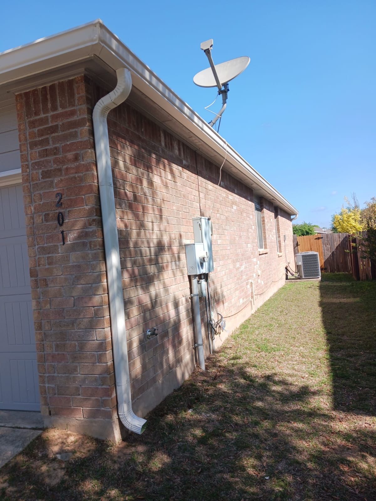 Brick house exterior with white gutters, garage, and satellite dish under a blue sky.