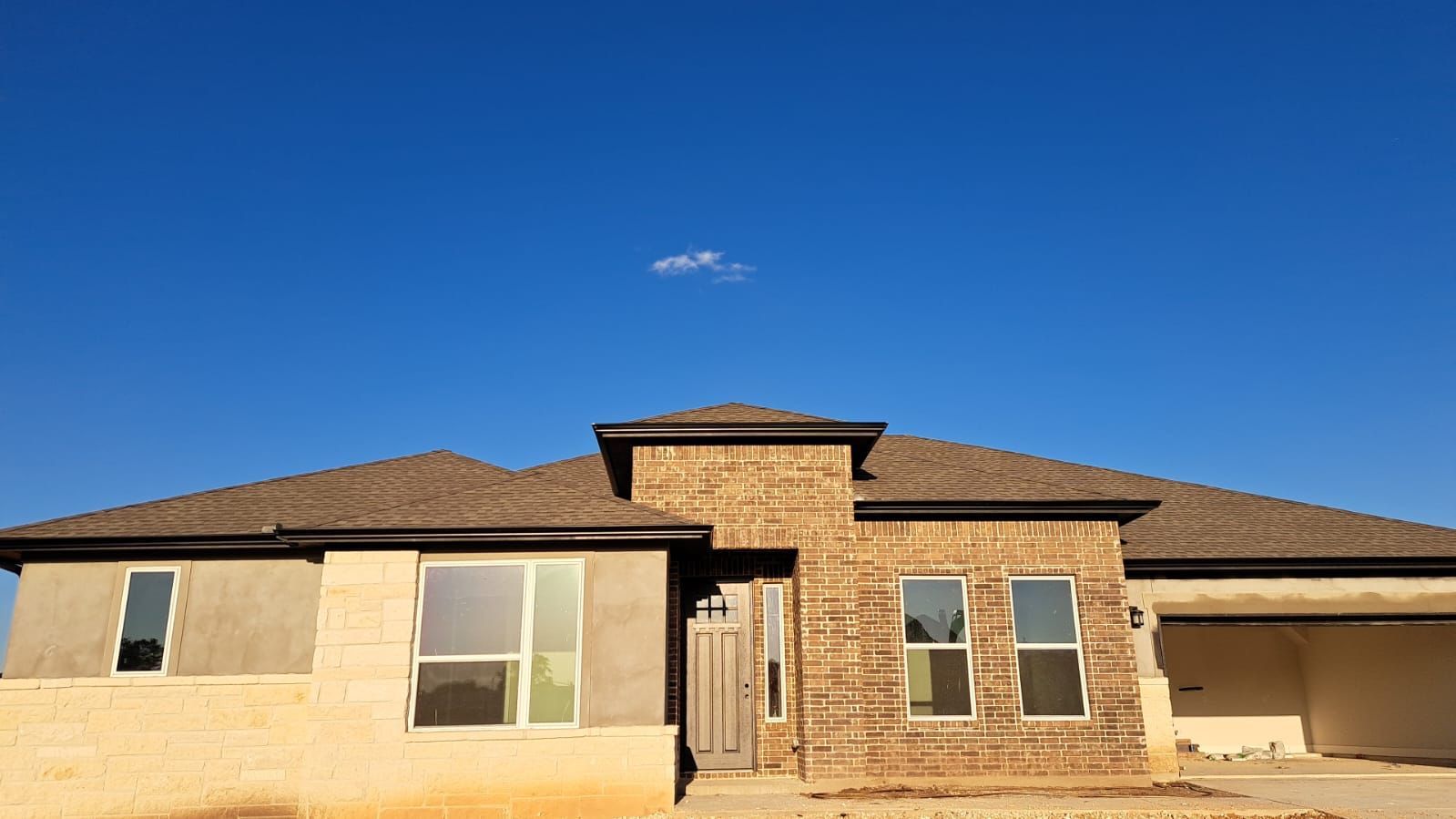 New construction house with brown roof and brick facade against a blue sky.