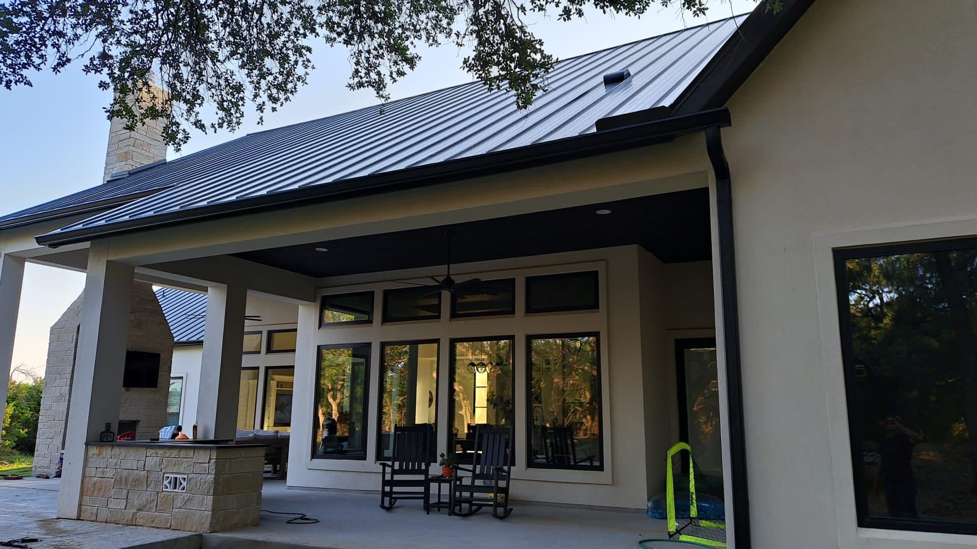 Back patio of a house with black roof and trim, large windows, and stone accents.