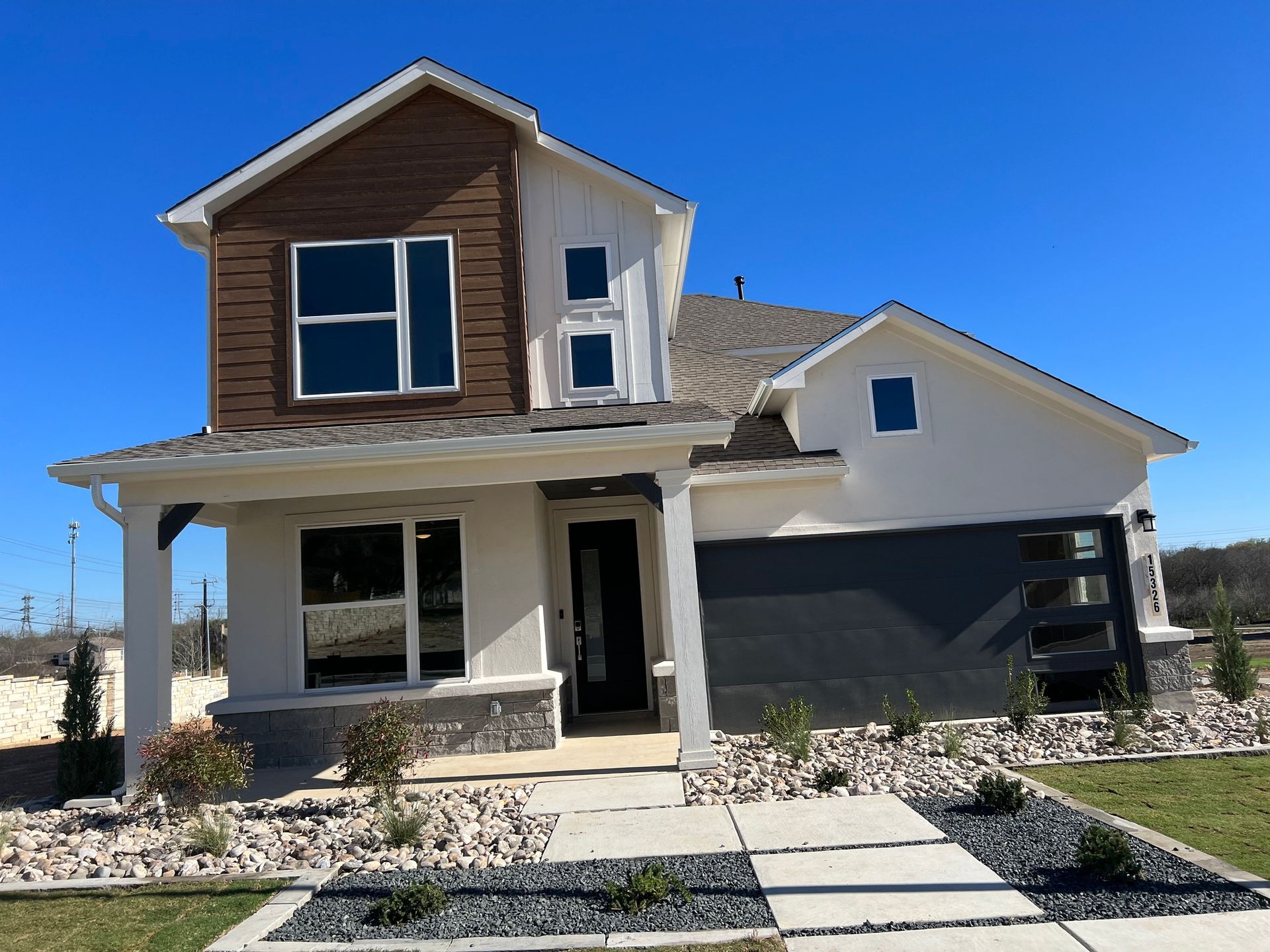 Two-story modern home with white and brown exterior, dark garage door, and stone walkway.