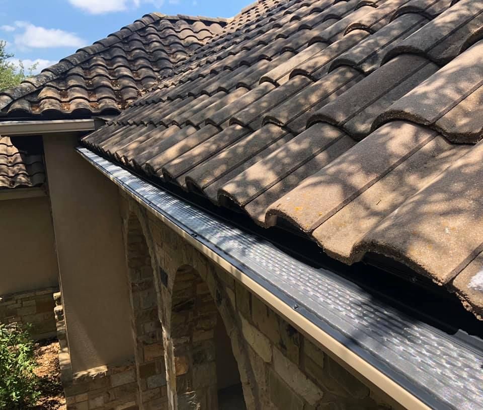 Close-up of roof with brown tiles and a gutter system; sunlight casts shadows.
