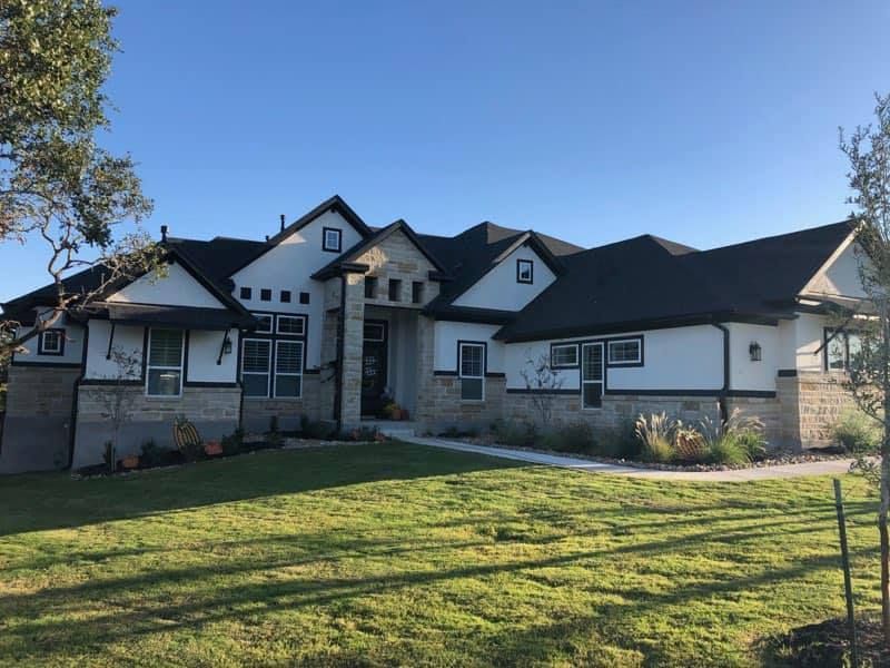 Large, two-story house with a black roof, white exterior, and stone accents under a clear blue sky.