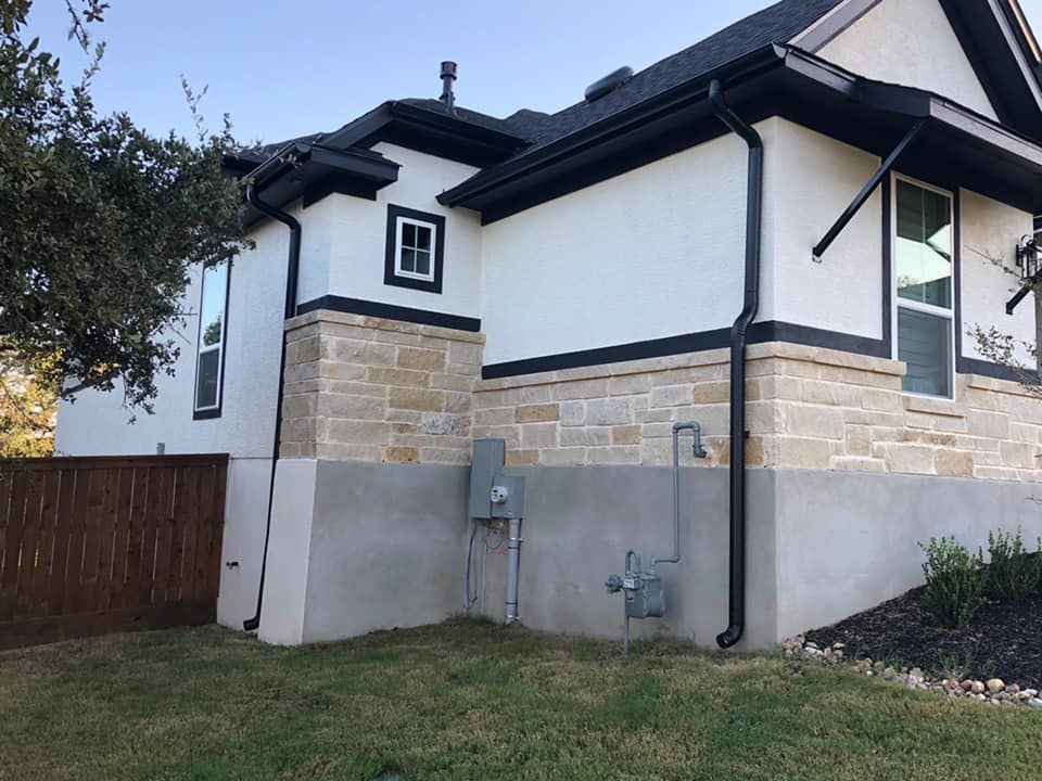 Exterior view of a house with white stucco walls, black trim, and stone accents.