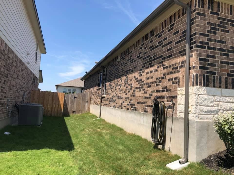 Side yard between two brick houses, with a wooden fence, green grass, and blue sky.
