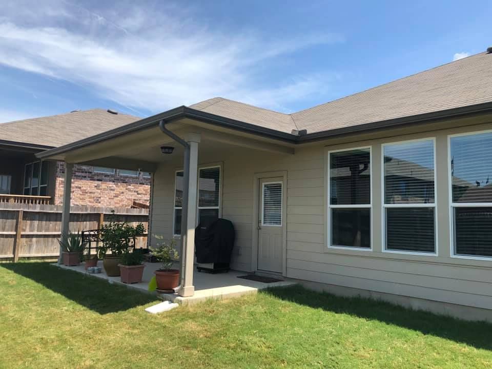 Beige house with covered patio, grass lawn, and wooden fence on a sunny day.