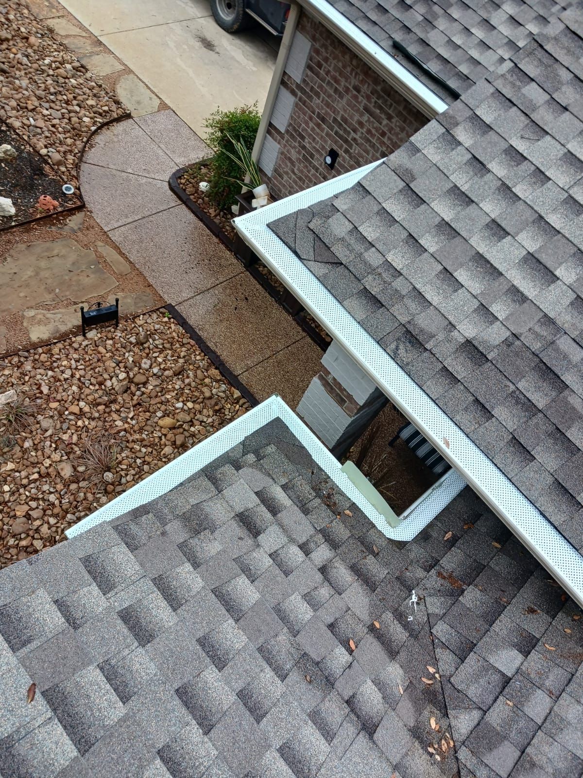 View of a house roof and gutters. Walkway with rocks and a small tree in the yard.