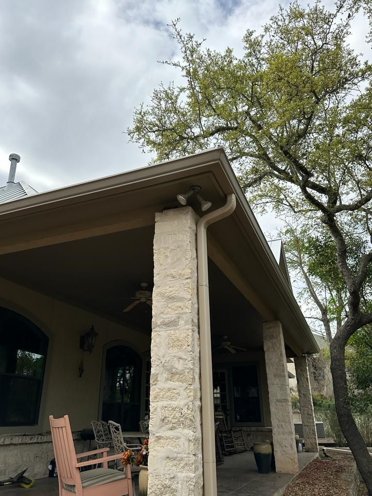 Covered porch with stone columns and a large tree against a cloudy sky.